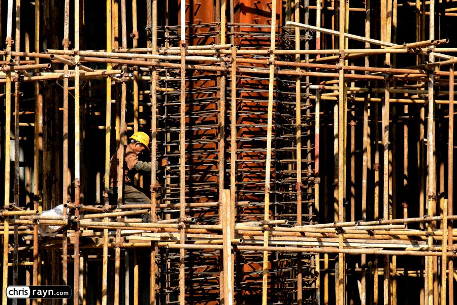 Construction worker kneeling at giant steel column amidst sc