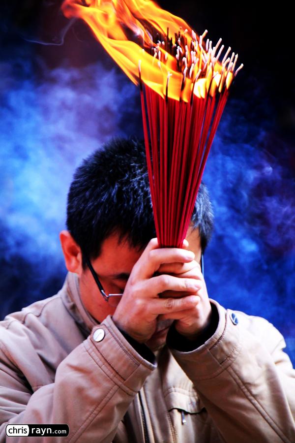 Catching fire, a praying man holds his joss sticks tight