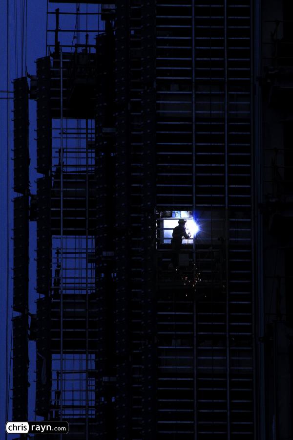 A lone welder illuminates a skyscraper at night