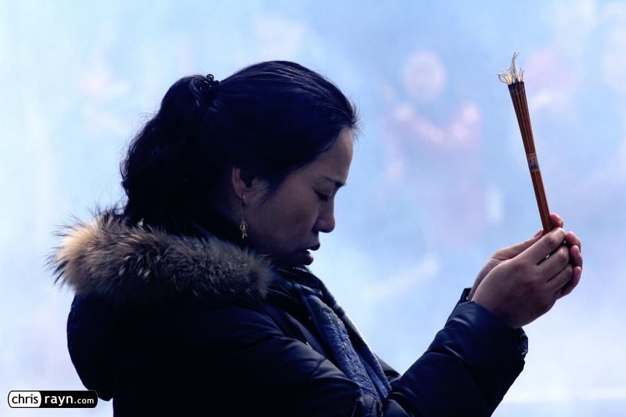 A praying woman in front of a wall of smoke in the temple